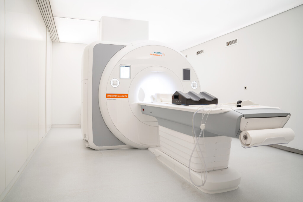 An MRI machine in a clean, white hospital room, with the patient table extended and medical equipment nearby, ready for use.