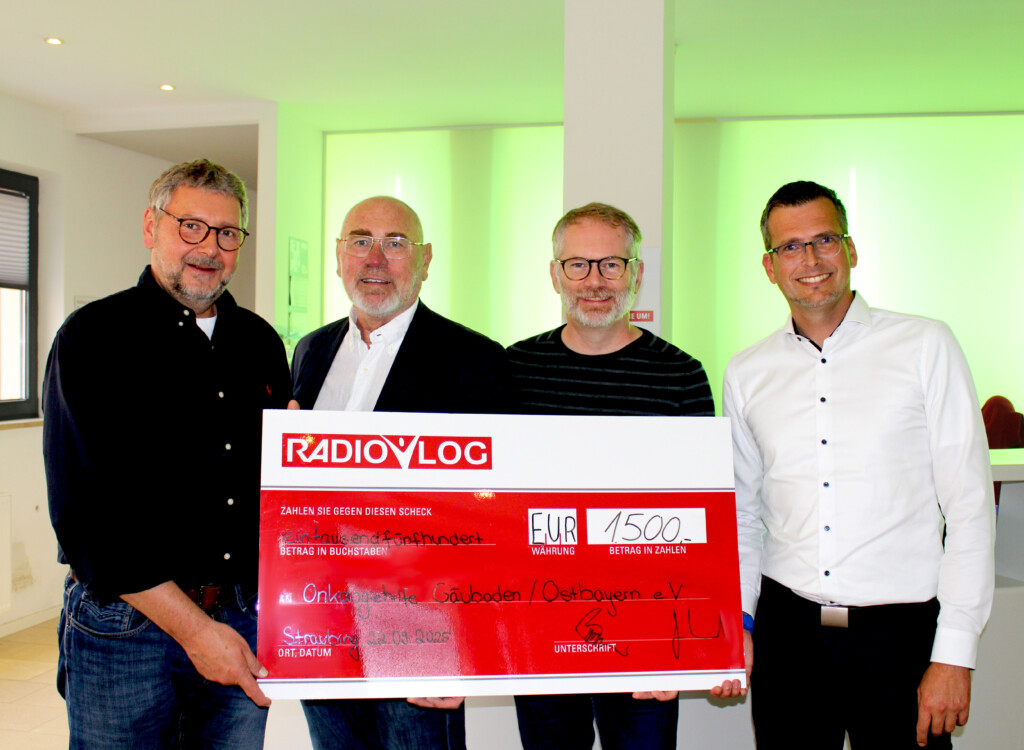 Vier Männer überreichen gemeinsam einen großen RADIO-LOG-Spendenscheck über 1.500 € für wohltätige Zwecke.