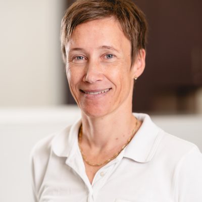 Portrait Stang-Coqui Dr. med. Alexandra Stang-Coqui, Ärztin bei RADIO-LOG in Bayern, steht in einem Innenraum und lächelt freundlich in die Kamera; sie trägt eine weiße ärztliche Kleidung mit Namensschild - das Bild vermittelt den patientenorientierten und kompetenten Ansatz des multidisziplinären RADIO-LOG Teams in der medizinischen Versorgung.
