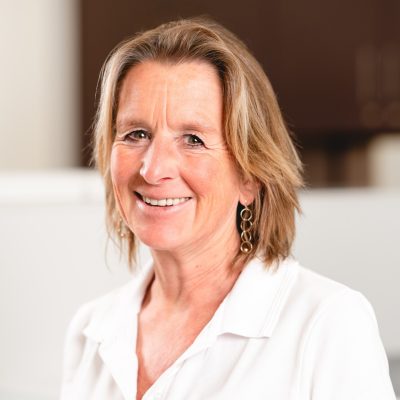 DSC01061-Bearbeitet-Bearbeitet Dr. med. Kathrina Huber, eine Ärztin von RADIO-LOG, lächelt freundlich in die Kamera. Sie trägt ein weißes Hemd und goldene Ohrringe; im Hintergrund ist eine helle Innenraumkulisse erkennbar. Das Bild vermittelt die vertrauensvolle und patientenorientierte Atmosphäre des medizinischen Versorgungszentrums RADIO-LOG in Bayern, das sich durch interdisziplinäre Zusammenarbeit und wohnortnahe Betreuung auszeichnet.