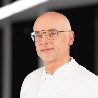 Dr. med. Ulrich Krause, Arzt im weißen Kittel, blickt freundlich in die Kamera; Foto für RADIO-LOG Bayern Webseite.